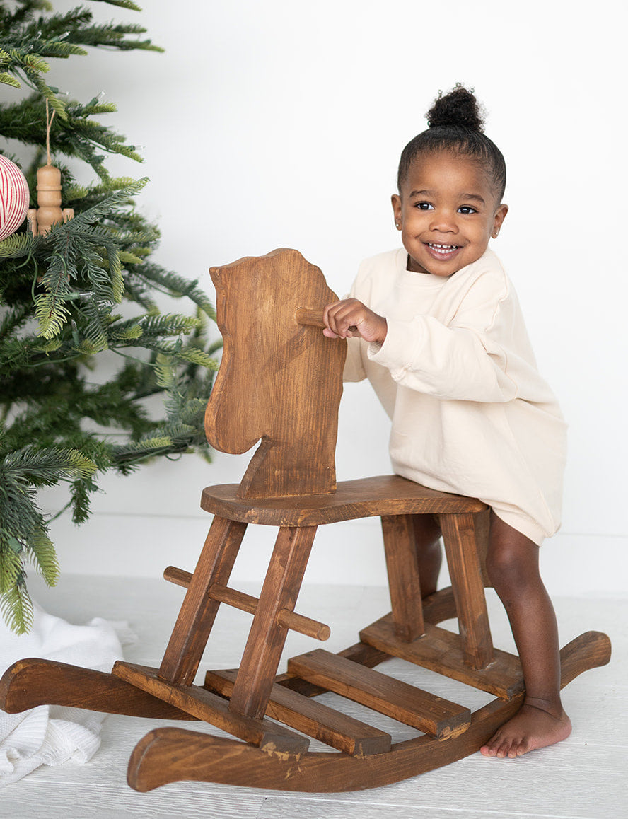 Child sitting on a wooden rocking horse with a Christmas tree in the background